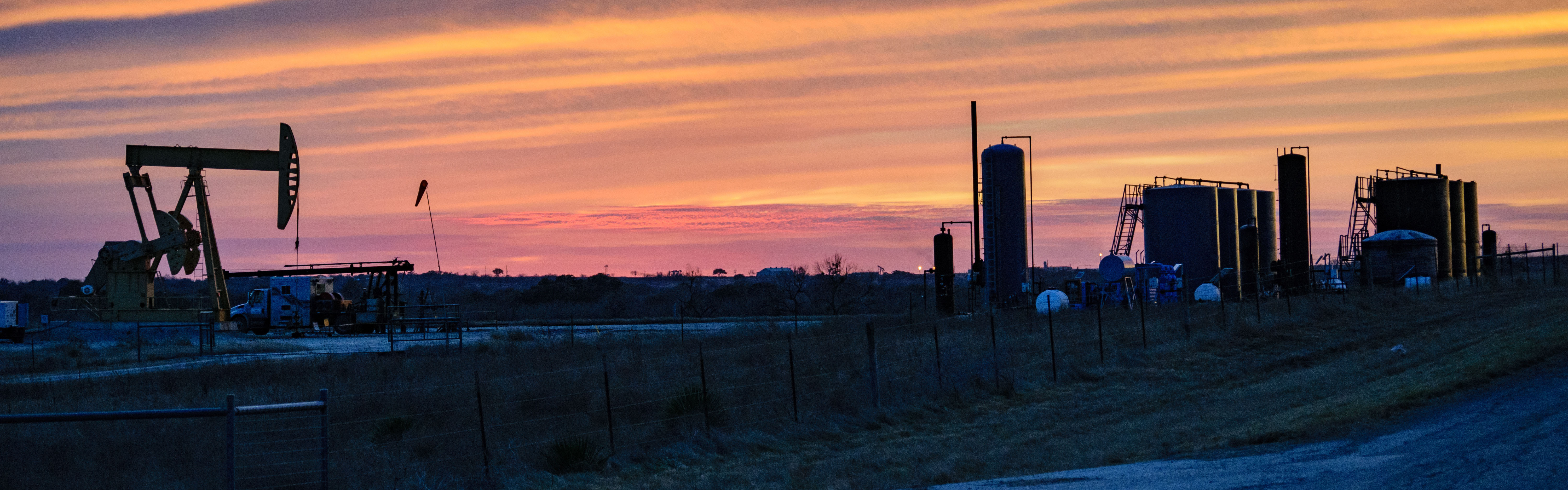 Oil and gas pump in field at sunset