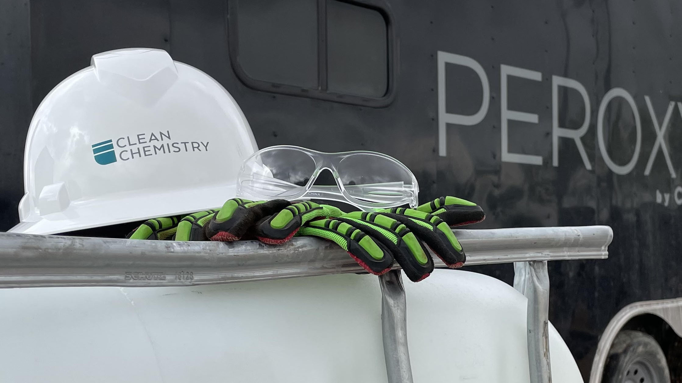 A hardhat, safety glasses and gloves sit on a tote in front of a PeroxyMAX trailer