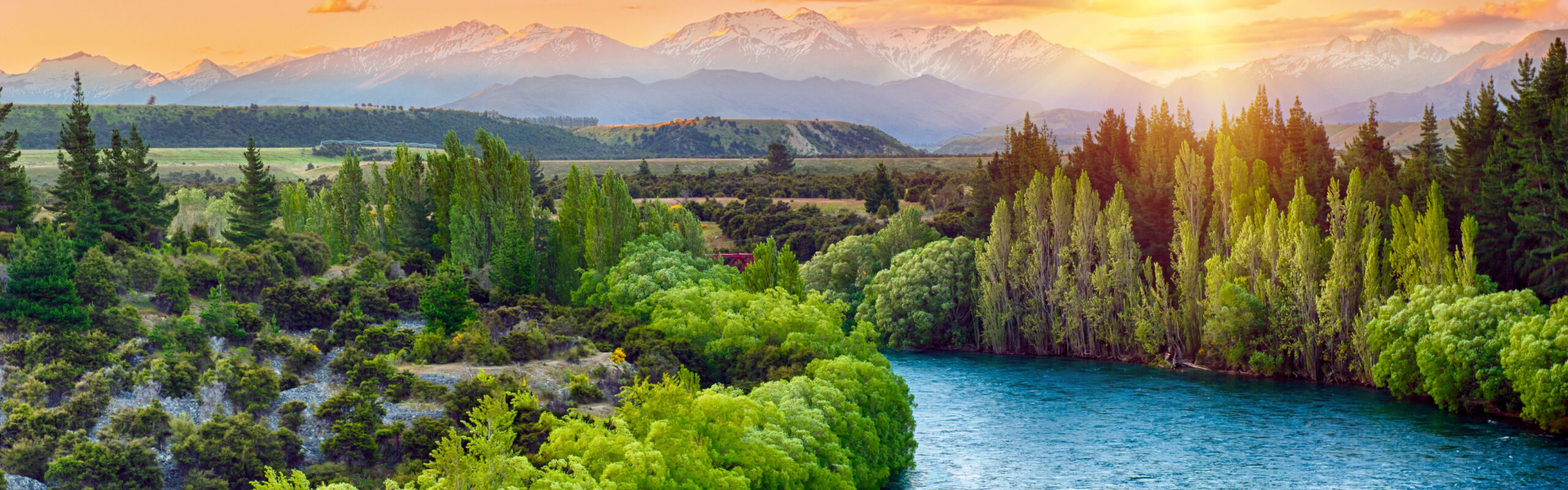 A clean river flows through a lush valley, with mountains in the background